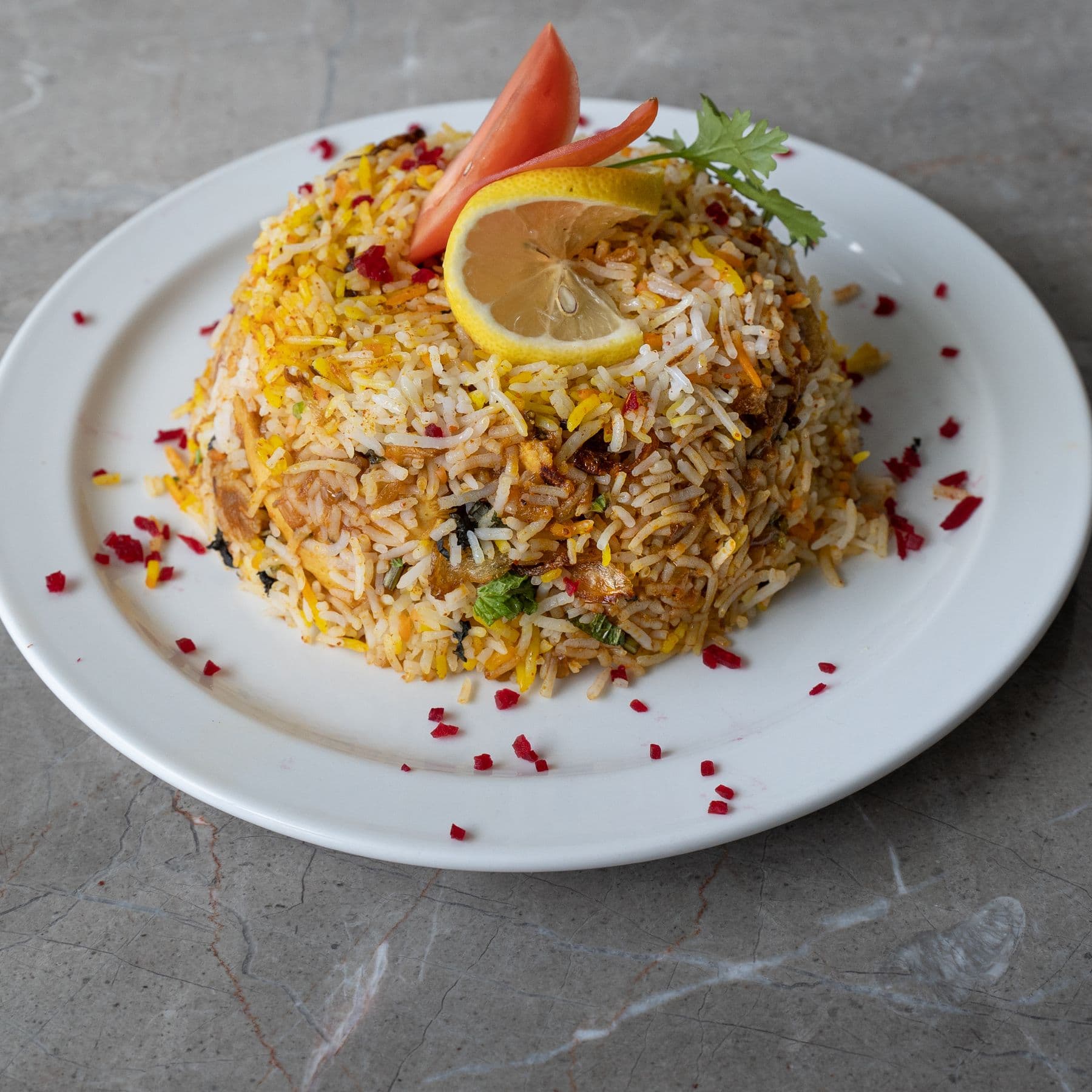 A plate of saffron biryani garnished with lemon and tomato